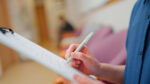 Clinician writes notes on a clipboard during a patient assessment.