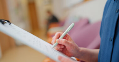Clinician writes notes on a clipboard during a patient assessment.