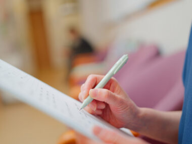 Clinician writes notes on a clipboard during a patient assessment.
