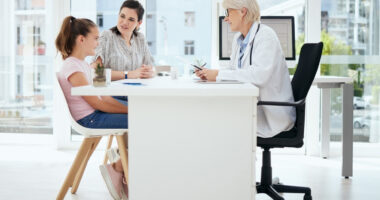 A doctor sits at a desk across from a young patient and their parent.