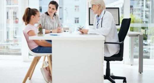 A doctor sits at a desk across from a young patient and their parent.