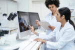 Two researchers in lab coats are seen using computers to analyze data.
