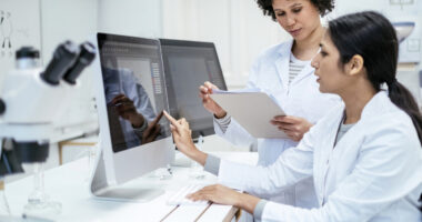 Two researchers in lab coats are seen using computers to analyze data.