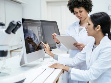 Two researchers in lab coats are seen using computers to analyze data.