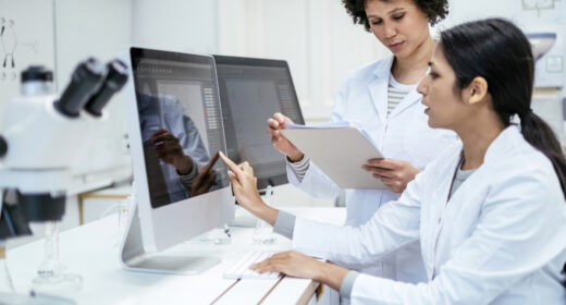 Two researchers in lab coats are seen using computers to analyze data.