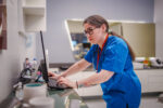 A healthcare worker stands at a counter looking at a computer screen.