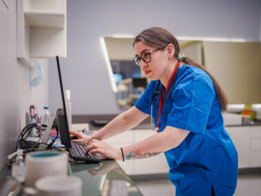 A healthcare worker stands at a counter looking at a computer screen.
