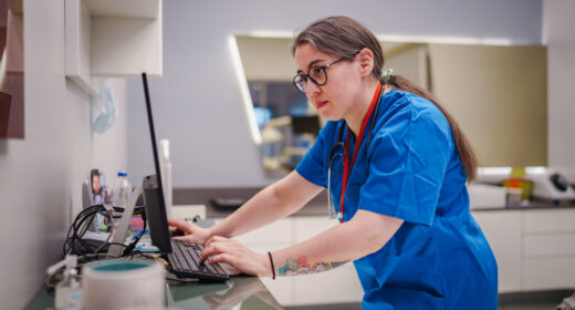 A healthcare worker stands at a counter looking at a computer screen.