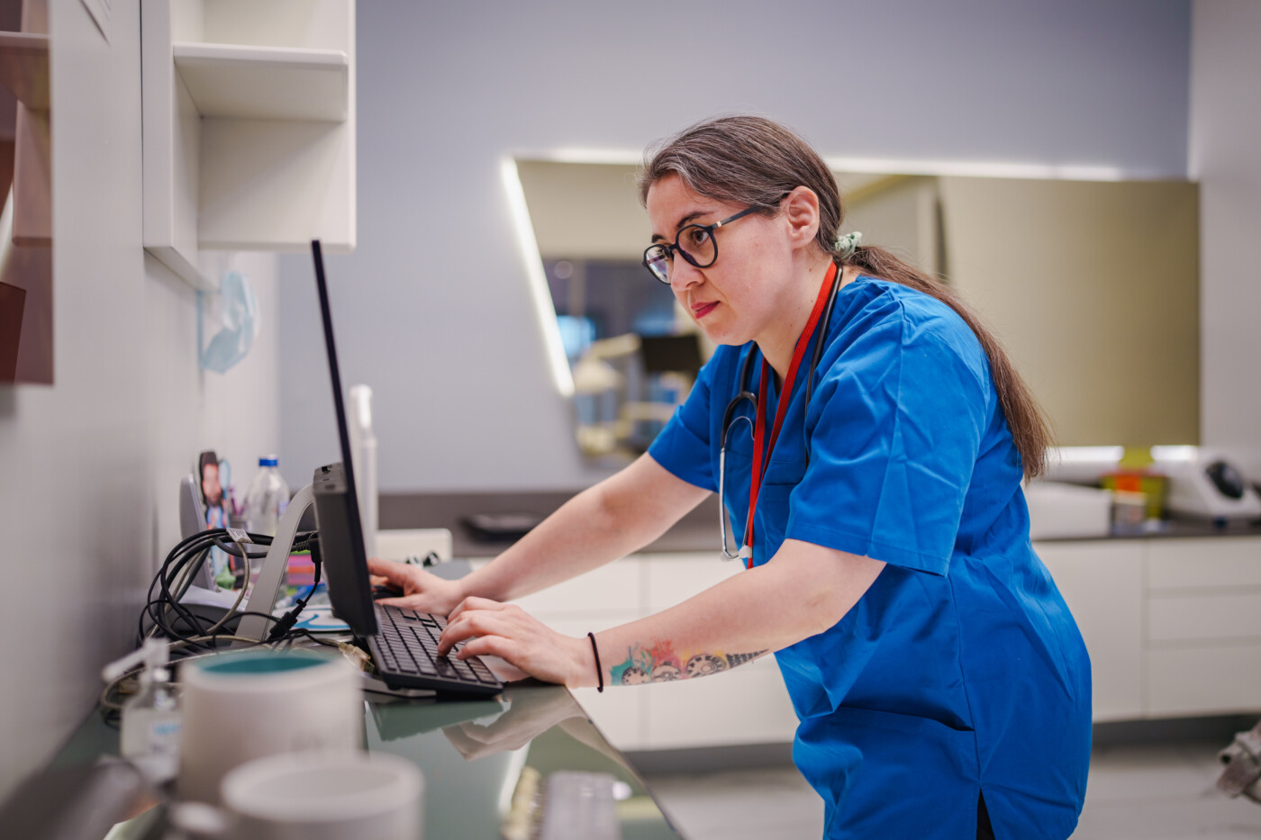 A healthcare worker stands at a counter looking at a computer screen.