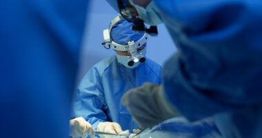 Surgeons wearing virtual reality headsets and surgical attire perform an operation.