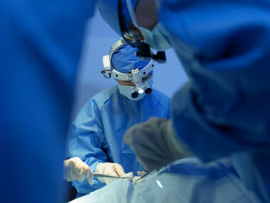 Surgeons wearing virtual reality headsets and surgical attire perform an operation.