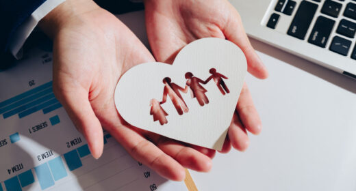 A pair of hands hold a heart-shaped piece of paper with cutouts of figures representing family and symbolizing love and care.