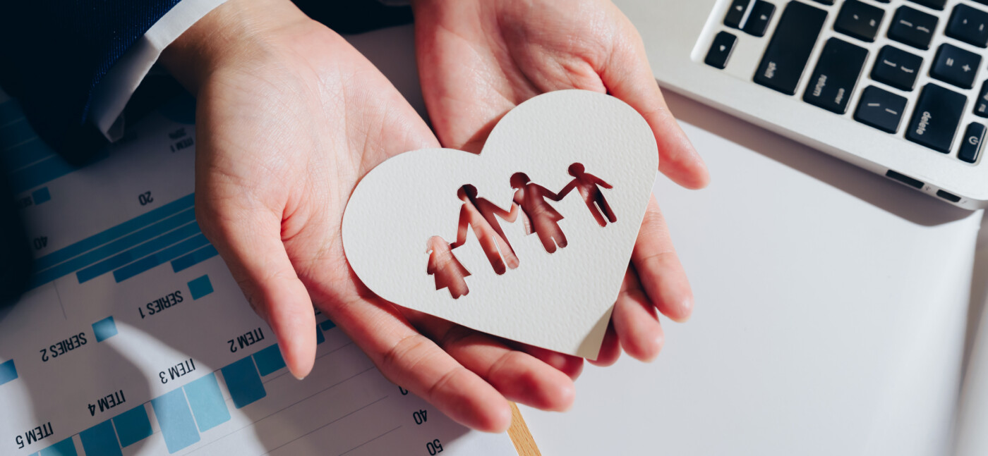 A pair of hands hold a heart-shaped piece of paper with cutouts of figures representing family and symbolizing love and care.